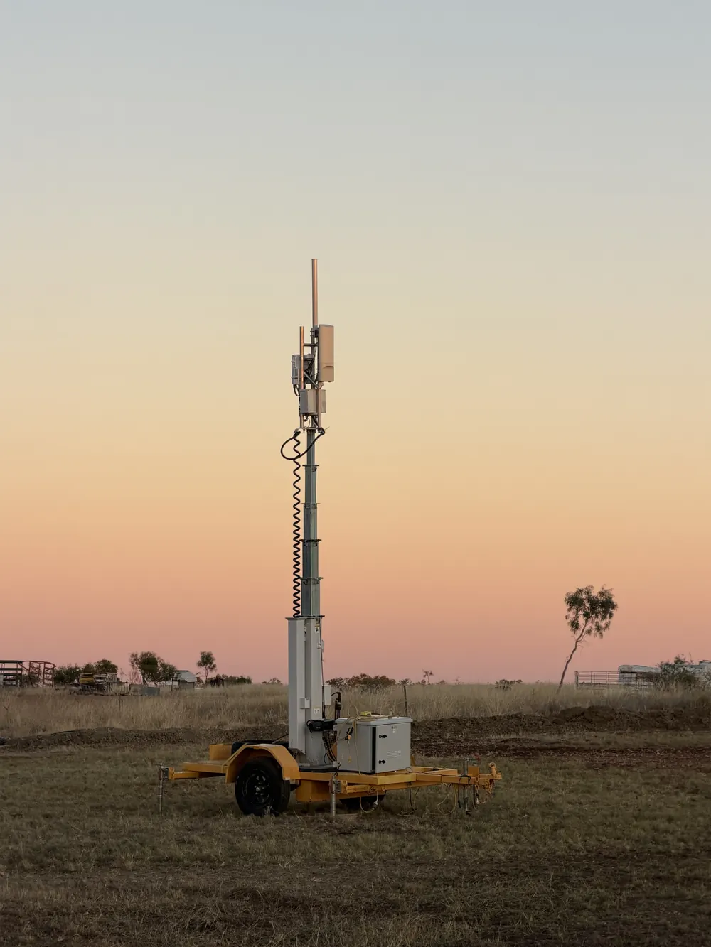 A Sky5G trailer-mounted mast raised on open ground under a pale dusk sky